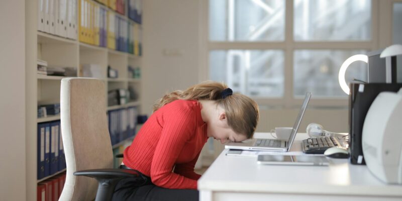 woman in red long sleeve shirt sitting on chair while leaning on laptop